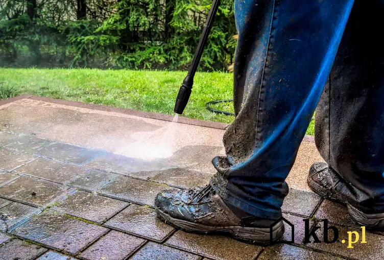Mycie kostki brukowej myjką pod wysokim ciśnieniem przez mężczyznę w stroju roboczym i ubłoconych butach