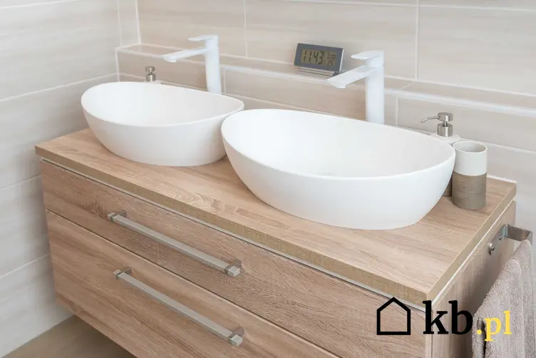 Umywalki nablatowe na standardowej wysokości w bardzo nowoczesnym stylu na drewnianej komodzie łazienkowej na tle kremowych płytek
