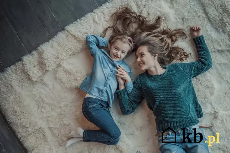 Kobieta i dziewczynka leżące na grubym dywanie w białym kolorze z firmy Kowary, a także najlepsze modele, ceny i rodzaje