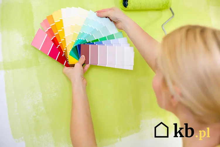 Paleta barw na tle malowanej ściany trzymana przez kobietę. Farby Luxens i ich rodzaje, ceny oraz zastosowanie