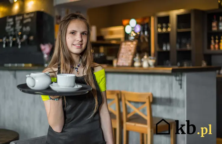 Młoda dziewczyna stojąća z tacą w kawiarni, młody pracownik dorabiający w kawiarni, jaką umowę podpisać z niepełnoletnim pracownikiem, wynagrodzenie dla ucznia za wykonaną pracę