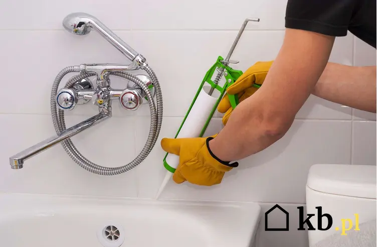 Mężczyzna silikonujący przestrzenie między umywalką a okładziną ścienną, o czym warto pamiętać remontując łazienkę