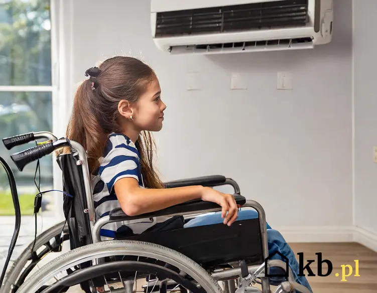 Dziewczynka siedząca na wózku inwalidzkim; w tle widoczna zamontowana na ścianie klimatyzacja.