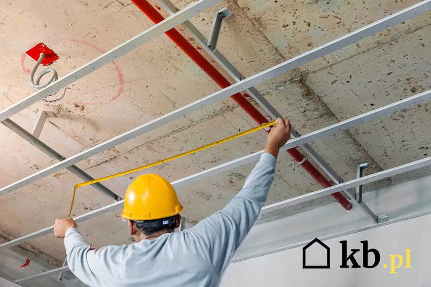 Systemy wodne i elektryczne, które w wielu przypadkach montuje się w sufitach podwieszanych, mogą ograniczać wysokość pomieszczeń Mężczyzna montuje sufit podwieszany