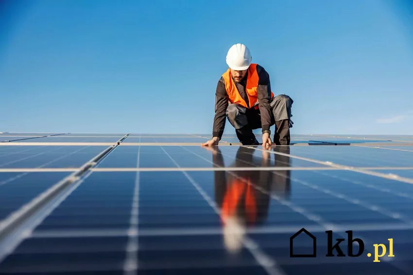 Nowy system rozliczeń za energię z fotowoltaiki zmniejsza opłacalność instalacji on-grid Młody mężczyzna w kasku montuje panele fotowoltaiczne na dachu