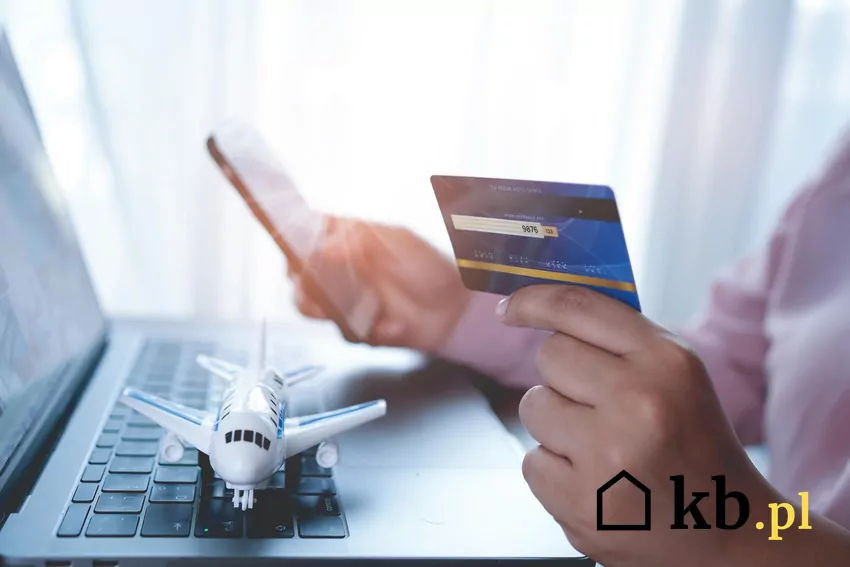Przed lotem warto zorientować się, jakie rodzaje płatności są aktualnie akceptowane przez wybranego przewoźnika Mężczyzna trzyma w dłoniach telefon i kartę, obok leży laptop i makieta samolotu