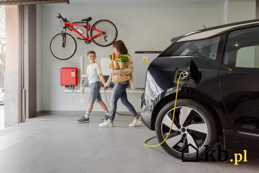 Samochód elektryczny podpięty do ładowania w garażu i dwoje ludzi