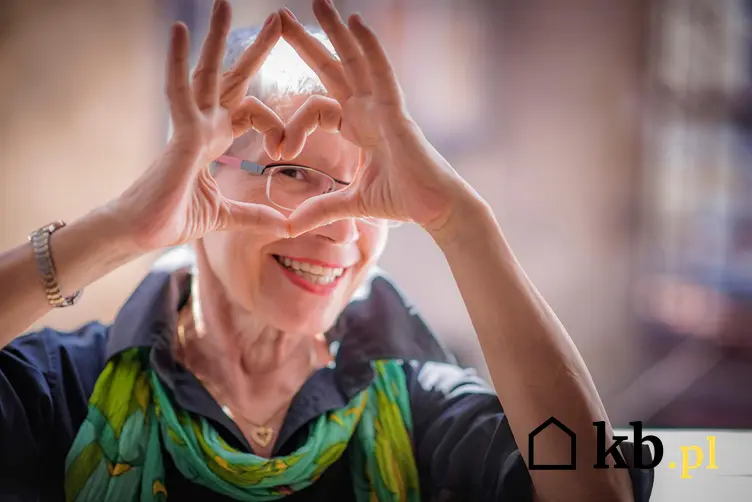 Uśmiechnięta emerytka pokazująca palcami symbol serca.
