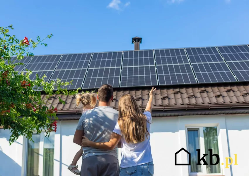 rodzina stoi przed domem z panelami PV na dachu