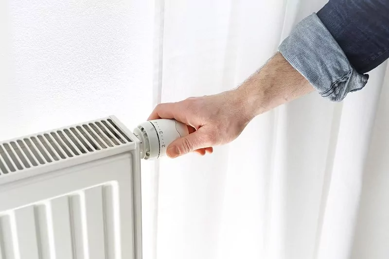 mężczyzna reguluje ciepło grzejnika