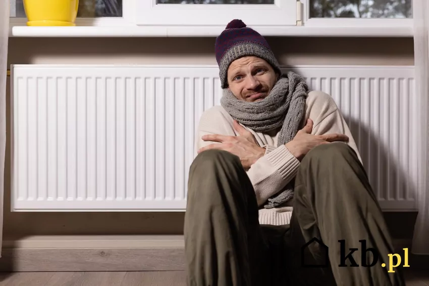 mężczyzna w szpiku i czapce siedzi przy grzejniku