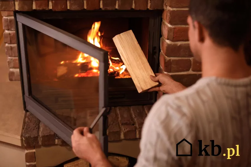 mężczyzna wkłada drewno do paleniska kominka
