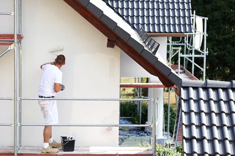 Jasna elewacja odbija więcej promieniowania słonecznego, co ogranicza nagrzewanie i wychładzanie ścian. mężczyzna malujący elewację na jasny kolor