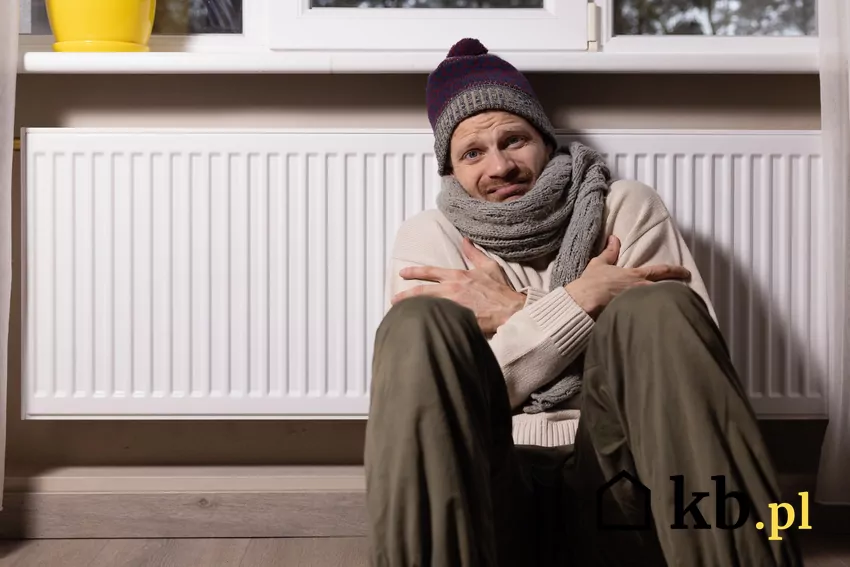 człowiek w czapce i szaliku siedzi obok kaloryfera