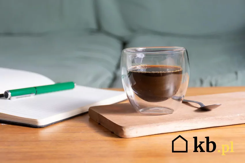 Kawa zaparzona w szkance na desce, obok zeszyt i długopis