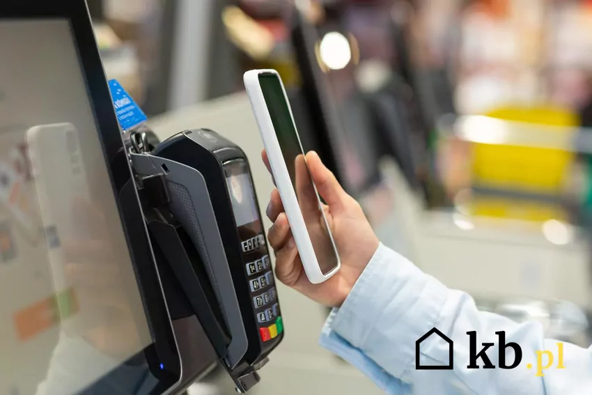 Klient przy kasie zbliża telefon do czytnika kart