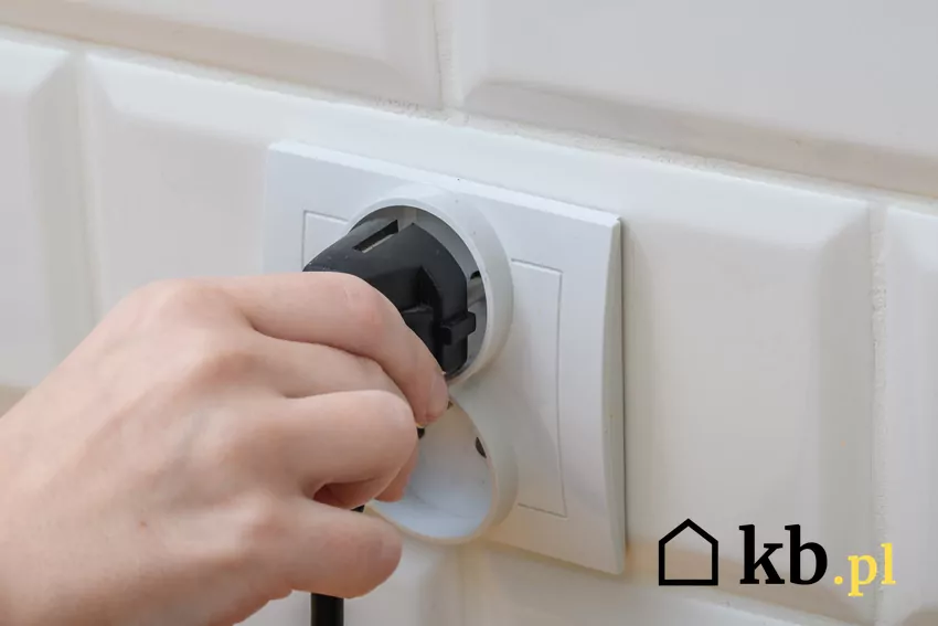 Prosumenci starają się zużywać najwięcej prądu w godzinach szczytowej produkcji energii z PV człowiek wkłada wtyczkę elektryczną do kontaktu
