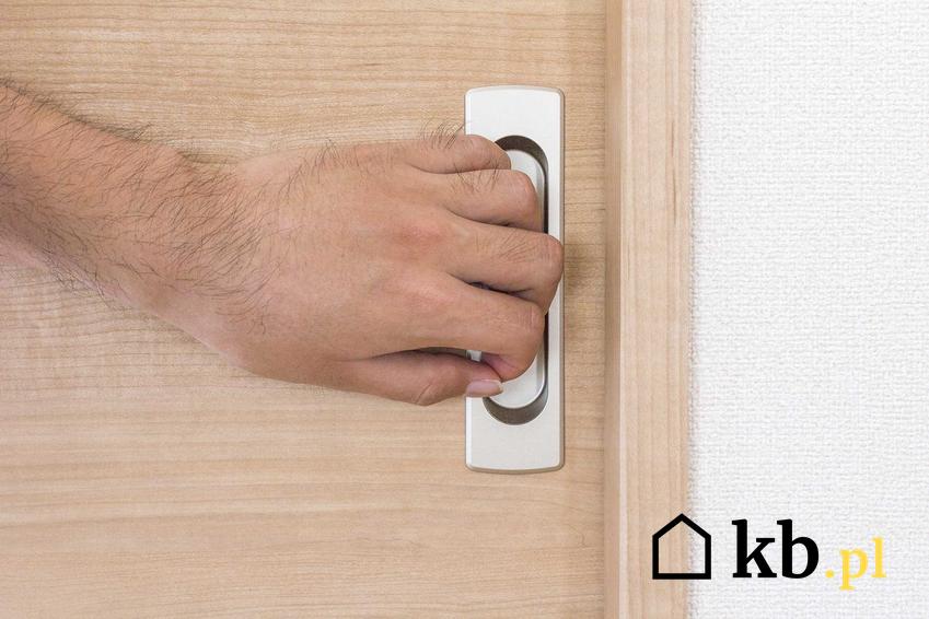 Męska dłoń na klamce drzwi przesuwnych. Drzwi przesuwne chowane w ścianę oraz możliwości ich zastosowania