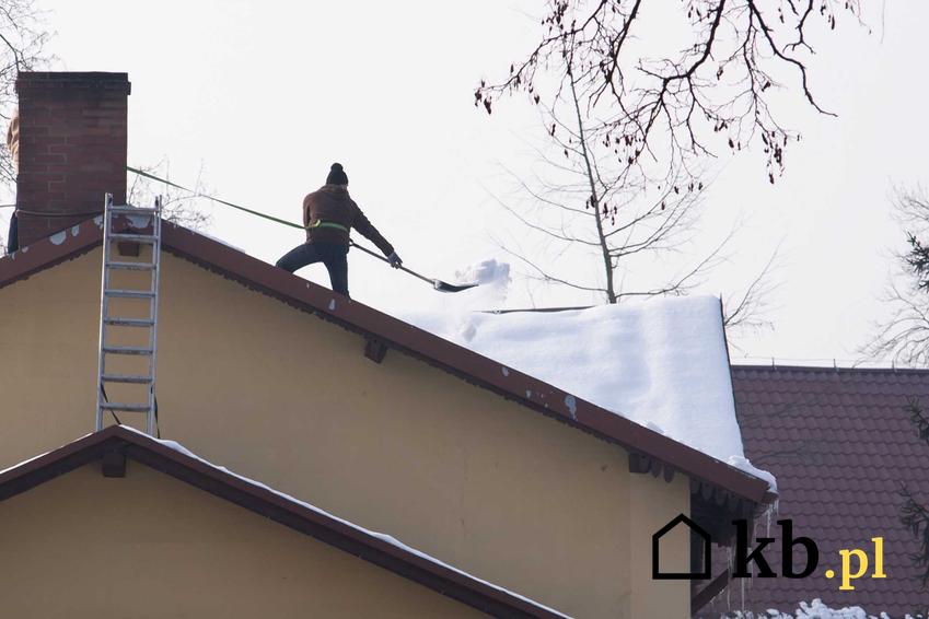 Mężczyzna podczas odśnieżania dachu zimą, a także najlepsze sposoby na odśnieżanie dachu i usuwanie śniegu z dachu krok po kroku