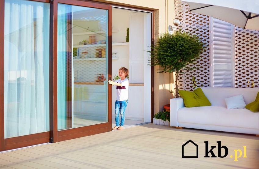 Drzwi tarasowe w brązowym kolorze i zamykające je dziecko, a także ceny, rodzaje i sposób montażu