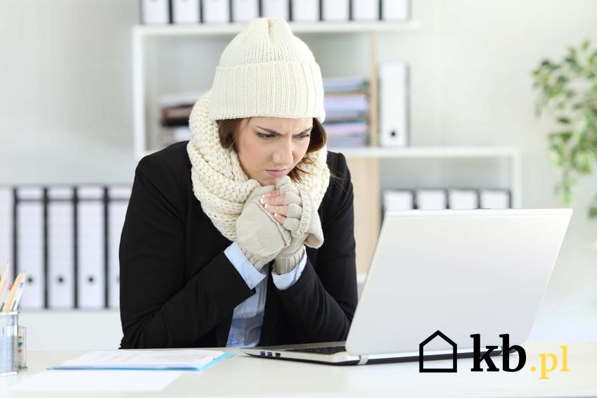 Kobieta w zimowej czapce i szaliku w biurze przy biurku, zimno w miejscy pracy, ile stopni powinno być w biurze