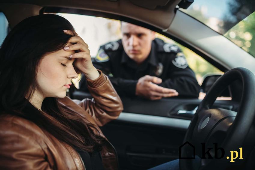 Kobieta siedząc w samochodzie trzyma się za głowę, a przez szybę zagląda policjant, zatrzymanie kierowcy przez policjanta, ile wynosi mandat za prowadzenie samochodu bez posiadania prawa jazdy