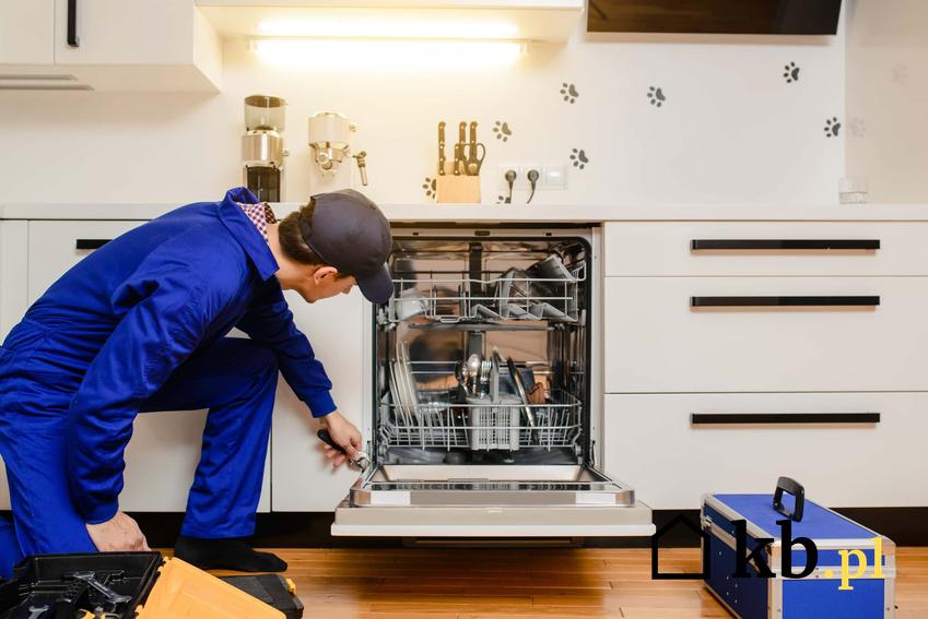 Mężczyzna w ubraniu roboczym montuje zmywarkę w kuchni, jak zamontować drzwi frotowe z abudowy do zmywarki, porady na temat montażu zmywarki pod zabudowę