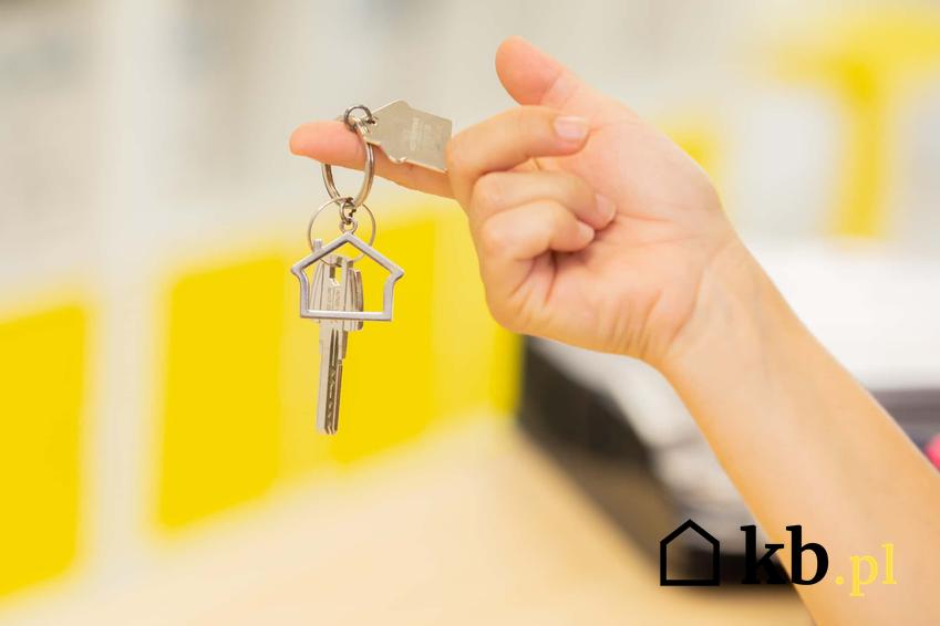 Dłoń trzymająca klucze od domu, klucz wiszący na palcu, co ma wpływa na wysokie ceny domów, jak tanio kupić mieszkanie