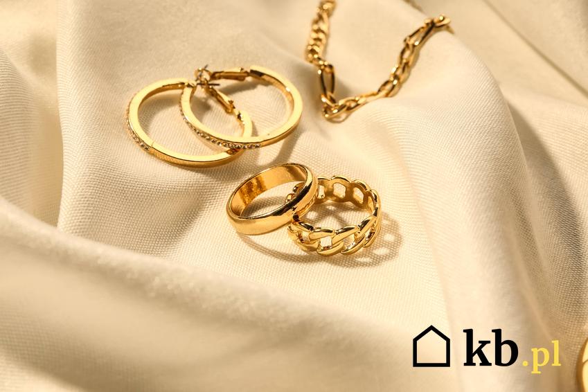 Złota biżuteria leżąca na eleganckiej tkaninie, a także porady, jak wyczyścić złoto domowymi sposobami